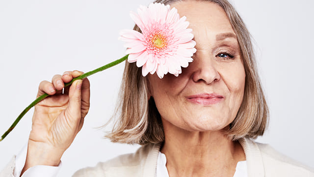 Ältere Frau hält sich eine Blume vor ein Auge